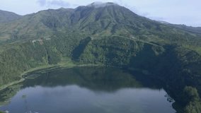 Fly over lake with mountain on the background. A large crater that became a lake. Menjer Lake, Indonesia.