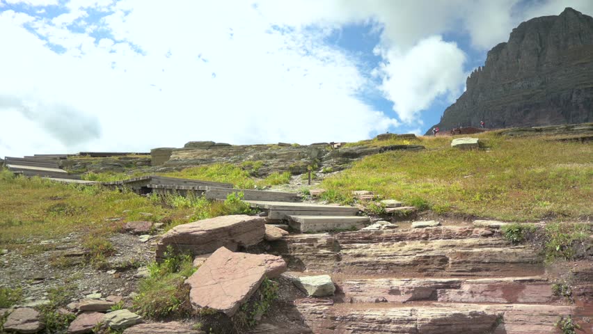 Hikers climbing stone stairs on Hidden Lake Trail in Glacier National Park with Mount Clements in the background, static