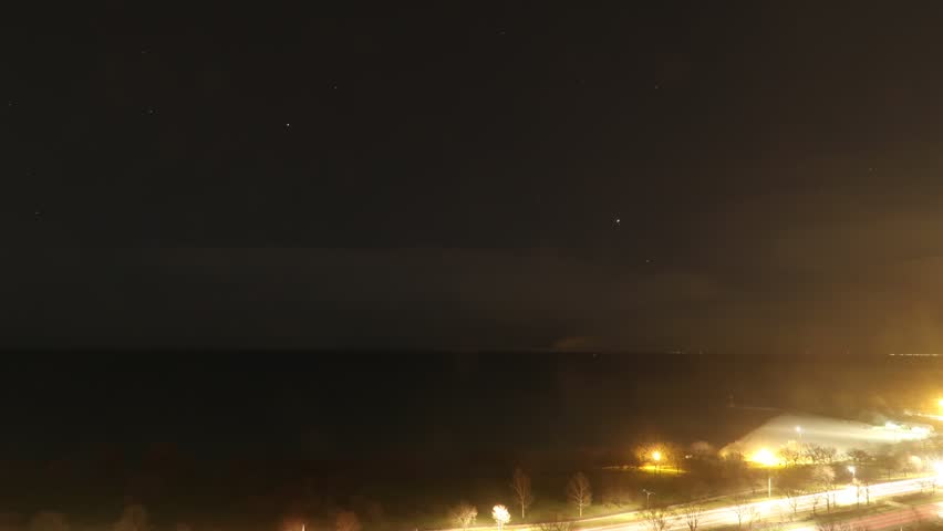Night time-lapse of star trails over Lake Michigan in Chicago with airplanes and clouds leaving their marks in the black night sky above and water below.