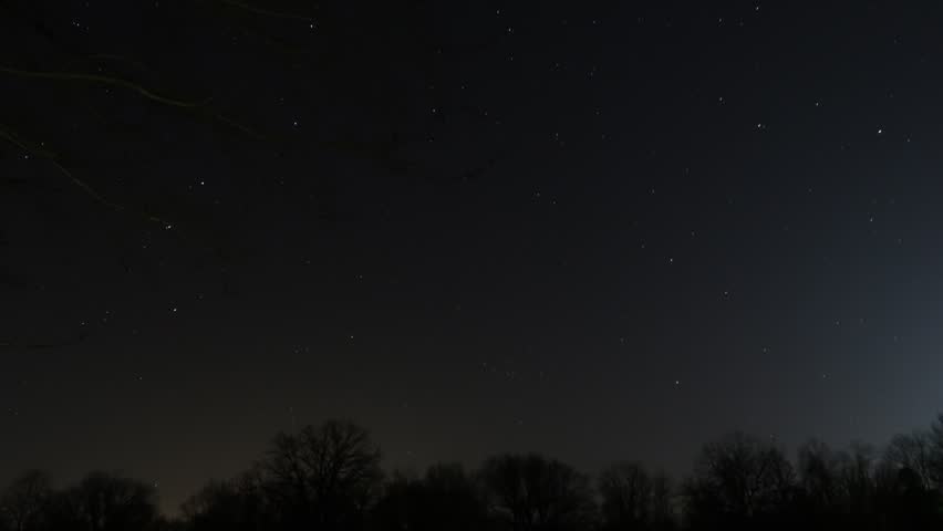 Night time lapse of continuous star trails looking up at the sky in Wisconsin showing the curved lines the stars travel as the earth rotates on a dark blue sky with view framed with trees.