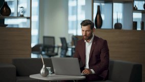 Confident smart ceo conducting video meeting with partners sitting modern office in elegant suit. Attractive bearded business consultant talking with company clients using laptop web camera at hall