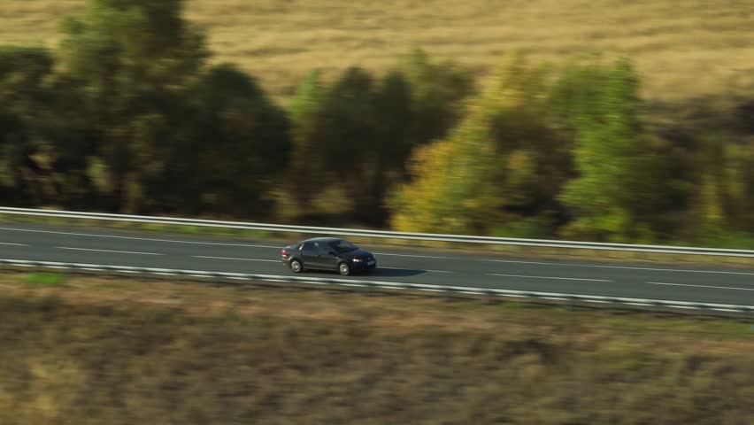 One black sedan car driving, travel on empty straight asphalt road freeway through empty arid steppe plain at summer sunny day. Aerial drone wide into the distance view.