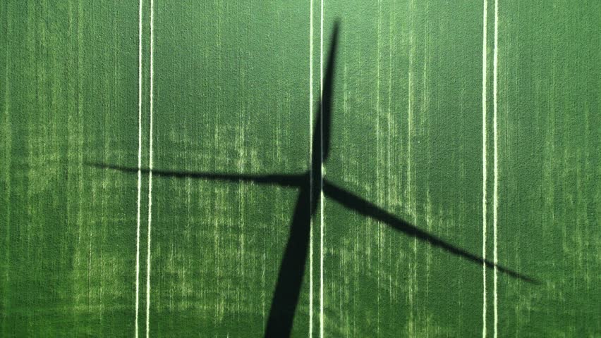 Shadow of a large wind generator on the green grass. Blades of the wind turbine are slowly rotating. Aerial view from above. Environmental protection, renewable energy sources. 4k footage