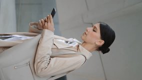 Serious businesswoman messaging by smartphone outside in elegant coat. Worried attractive woman reading bad news looking phone vertically video. Anxious company manager standing street with mobile.
