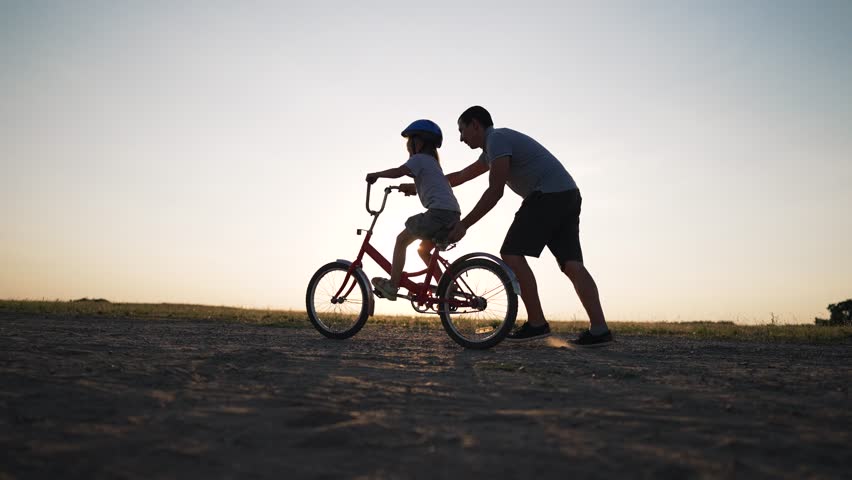 Happy family. Father teaches daughter to ride bike in park. Daughter riding bike for first time. Kid dream of traveling by bike. Girl is learning to ride a bike. Father helping hand to daughter Royalty-Free Stock Footage #3434381321