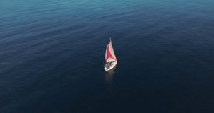White modern sailing yacht in blue warm water. A view from a drone of a ship with a sail plowing the depths of the ocean. Traveling by sea in the rays of the setting sun. Luxurious lifestyle
