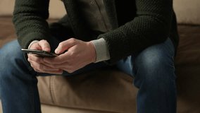 Man using smartphone, sitting on couch , close-up. Man using mobile phone at home scrolling through social media or online shop internet, communications concept, 4k slow motion
