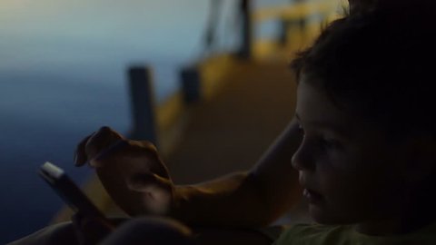 Woman standing with her son while using smartphone at night next to the sea
