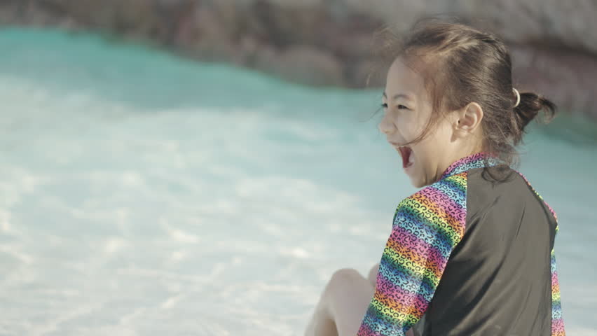 Half body of one adorable asian kid girl who is playing water in beautiful swimsuit in swimming pool in hotel resort during summer vacation with happiness, enjoyment and cheerfulness.