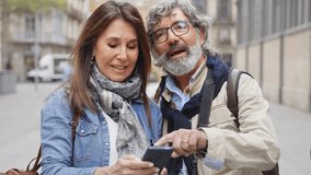 Senior couple of tourists looking map GPS navigation on smart mobile phone device - Husband and wife using cellular outside - Technology life style concept video 