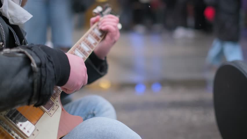 Close-up of a male music lover playing the guitar in a crowded city. 