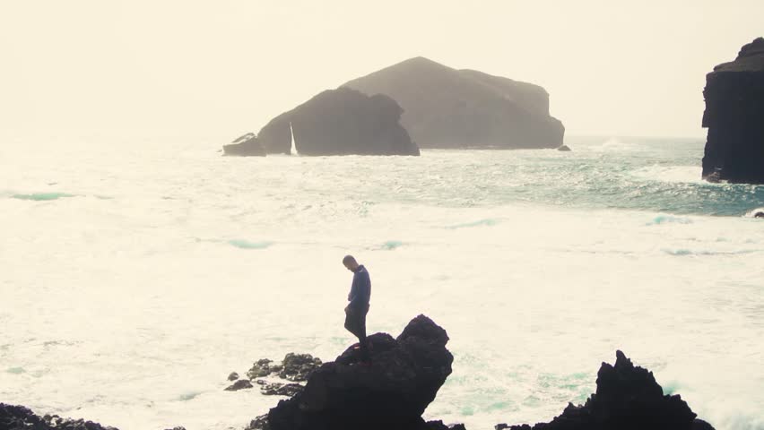 Man silhouette standing on rock with open arms against monsteiros beach in Sao Miguel, Azores Island.