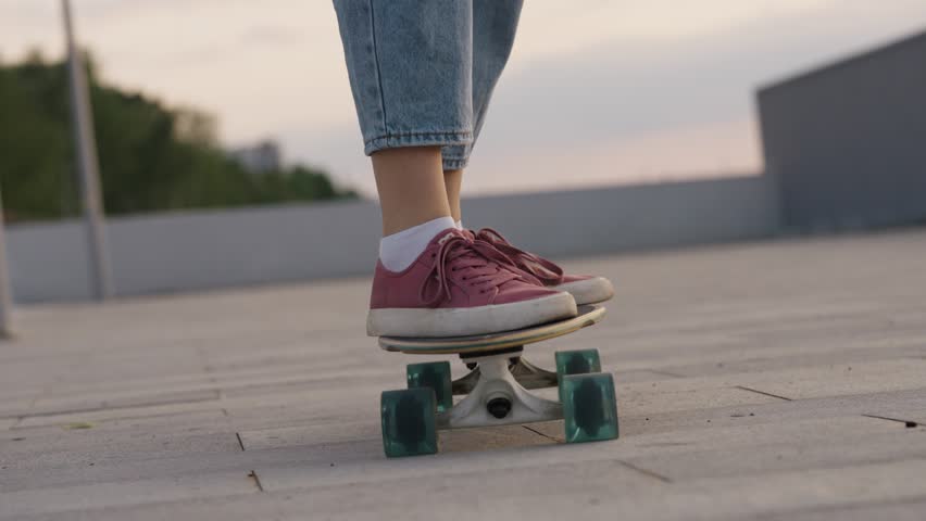 Close-up of a person's feet in red sneakers on a skateboard, cruising along a concrete pavement with a blurred urban background. Carefree teen girl riding a longboard on the waterfront Royalty-Free Stock Footage #3434619349