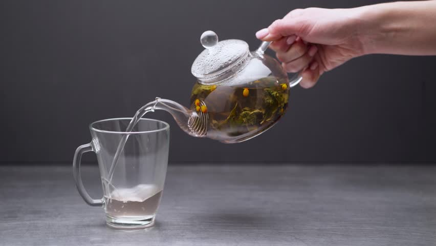 Tea with herbs and berries is poured into a transparent tea cup.