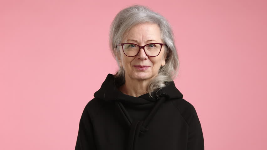 Amidst a rosy backdrop, a senior woman nods in agreement, her face lit with an approving smile, signaling a positive response in a serene setting. High quality 4k footage