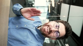 POV Vertical video. Smiling businessman in glasses talking on a video call using a smartphone in a office. Handsome manager waving hand looking at camera. Online chat with a client or business partner - Powered by Shutterstock - Get 15% off with code: PIKWIZARD15