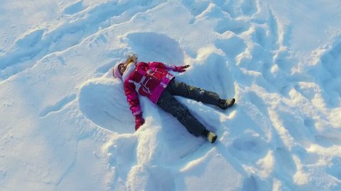 Kid making snow angel. Young cheerful girl lying on snow. Winter child fun. Beautiful girl playing in snow