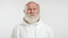 A video capturing an elderly man in a white hoodie touching his temple with a finger, making a crazy gesture, showing a humorous or sarcastic expression. Camera 8K RAW. 