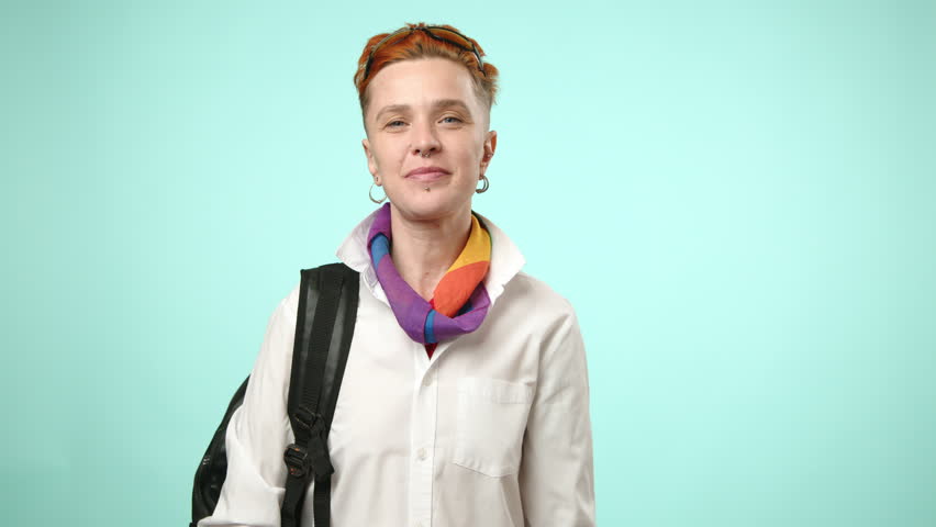 A lesbian student exudes joy while holding a tablet and wearing a backpack, her laughter and delight infectious against a soft blue backdrop. High quality 4k footage