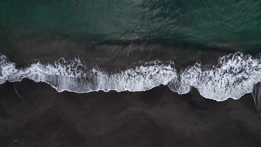 Waves breaking on black sand beach, Plage de Grande Anse bay, Guadeloupe, French Antilles. Aerial top-down sideways and space for copy
