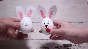 Full HD video for Happy Easter. White chicken egg with hare muzzle and bunny ears in female and male hand. People play egg battle. Concept of religion, holiday, kiss, competition, egg hunt. Wood table
