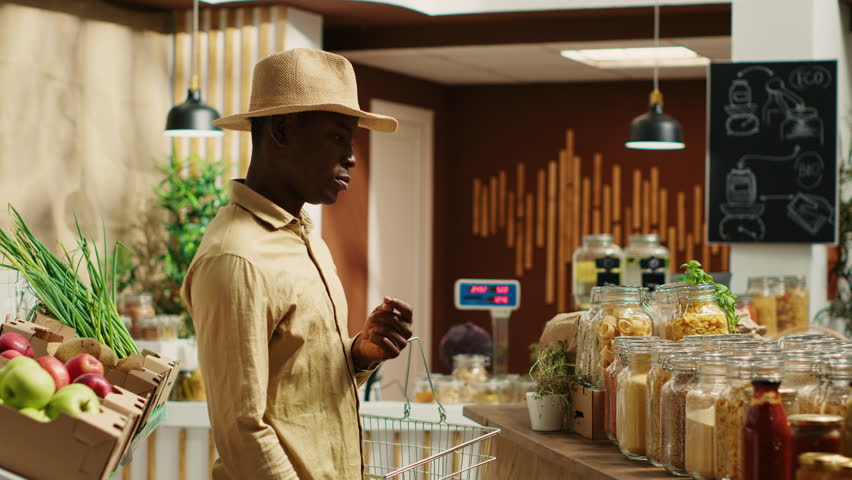 Client examines cereals and grains at zero waste eco store, looking for natural organic products and pantry supplies. African american man buying homemade spices and pasta in jars. Camera A.
