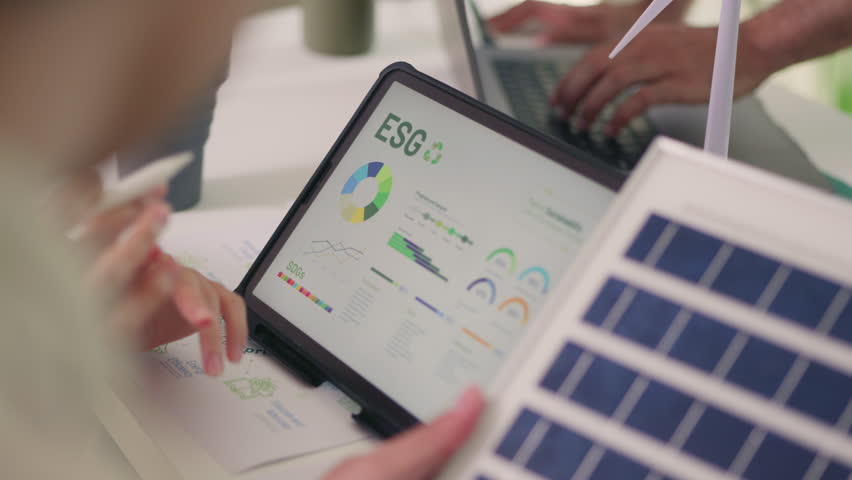 Over-the-shoulder view of a professional reviewing detailed ESG sustainability metrics on a digital tablet during a project meeting. - Powered by Shutterstock - Get 15% off with code: PIKWIZARD15