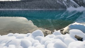 Winter at misty lake natural background footage. Cold icy moment. fluffy white snow front green emerald lake mountain scenery reflexed in clear water surface with cloudy blue sky at background. - Powered by Shutterstock - Get 15% off with code: PIKWIZARD15