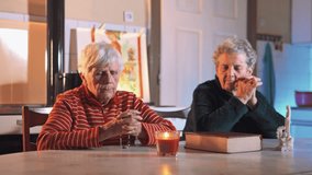 4K video of two elderly women praying next to the Holy Bible. Indoor scene with candle light.
