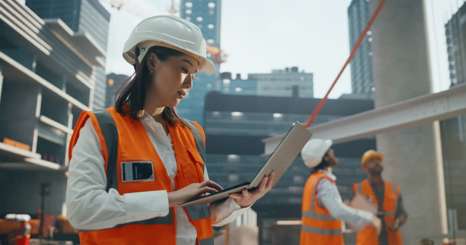 Portrait of a Beautiful Japanese Female Civil Engineer Working on a Laptop at a Construction Site. Young Asian Woman Standing Outdoors, Using Computer for Planning and Developing a Real Estate Project