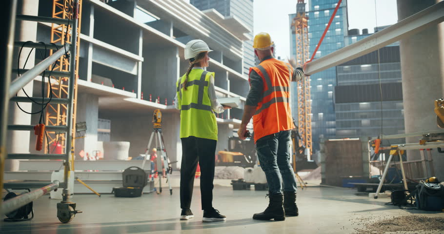 Professional Female Civil Engineer and a Construction Manager Having a Meeting to Discuss Project Plans of a Real Estate Building. Specialists Standing with Their Backs to Camera and Using a Laptop