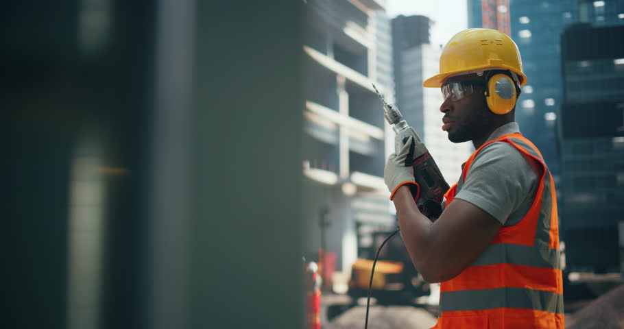 Portrait of a Handsome African General Worker Drilling Holes with a Power Tool at a Construction Site. Masculine Black Man Working with a Drill Outdoors, Preparing a Wall for Fabrication