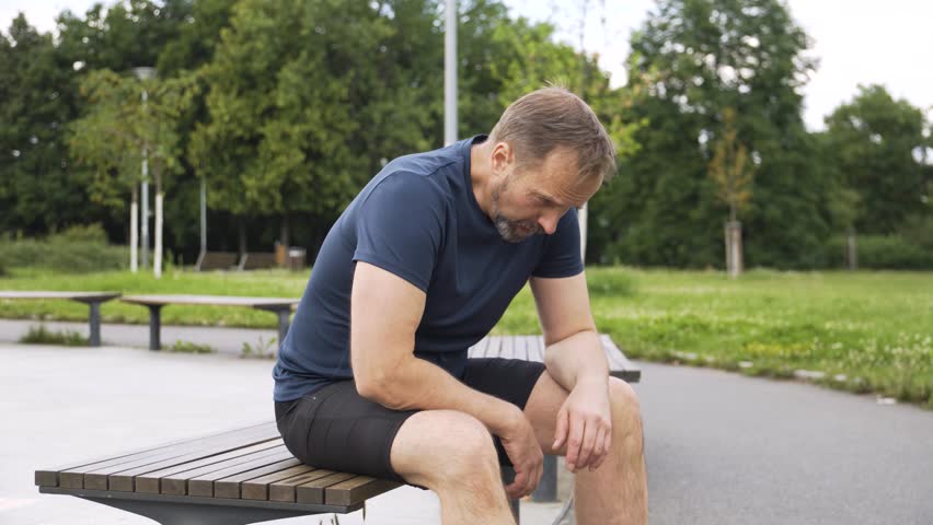A handsome middle-aged Caucasian man has a backache on a bench in a park