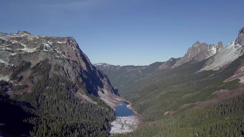 A drone slowly flys over a canyon between two mountains over an alpine lake in the pacific Northwest of Washington close to Canada