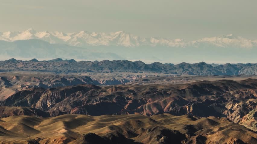 Mountainous terrain with beautiful skin rocky slopes with snow peaks background. Martian plateau landscape in Kazakhstan at summer sunny sunset.