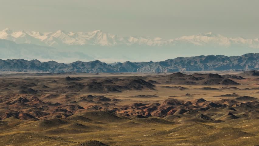 Mountainous terrain with beautiful skin rocky slopes with snow peaks background. Martian plateau landscape in Kazakhstan at summer sunny sunset.