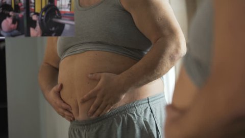 Plump man looking at muscular athlete on photo and touching his fat belly