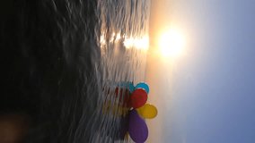 Bunch of multi-colored balloons tied with a ribbon floating on the surface of the sea water at sunset and dawn. Shining sun above the horizon at sunset and dawn. Slow motion - Powered by Shutterstock - Get 15% off with code: PIKWIZARD15