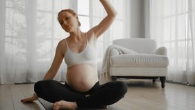 Pregnant woman doing pilates at home. Pregnant female doing yoga practice stretching with online lesson video training at home. Mother and child health relax and meditation exercise concept.
