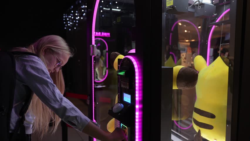 Young beautiful girl at the arcade trying to win big plush toy. Unsuccessful game. Emotional moment when girl loses. Royalty-Free Stock Footage #3435126179