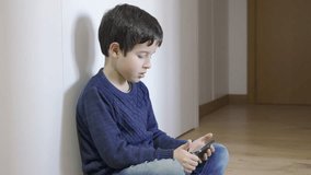 Lonely child with his phone. A little boy playing with a smartphone at home.