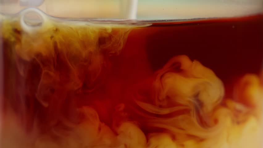 Milk pouring into coffee and liquid moving. Macro close up