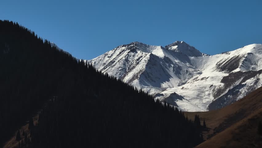 Mountains terrain with beautiful skin rocky slopes with snow peaks background. Alatau range in Kazakhstan at summer sunny sunset.