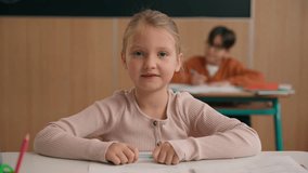 Portrait little Caucasian girl looking at camera primary school kid schoolgirl daughter child baby pupil student in class lesson studying education looking at camera sitting at table desk classmates - Powered by Shutterstock - Get 15% off with code: PIKWIZARD15