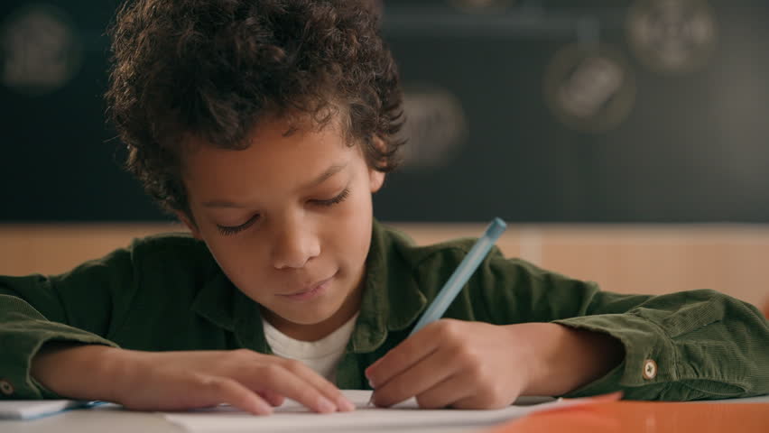 Little African American guy boy writing notes task class lesson primary school write in copybook kid schoolboy son child pupil student learning listen teacher studying education sitting at table desk Royalty-Free Stock Footage #3435217989