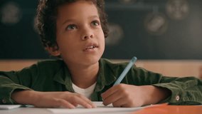 Little African American guy boy writing notes task class lesson primary school write in copybook kid schoolboy son child pupil student learning listen teacher studying education sitting at table desk - Powered by Shutterstock - Get 15% off with code: PIKWIZARD15