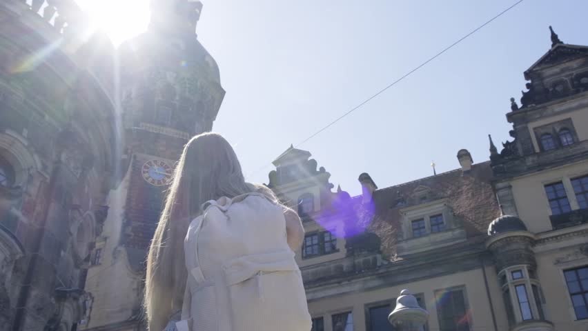 Woman walking near statue in city with buildings, sky, plants, and trees.