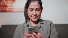 Asian woman sitting on bed using smartphone at home
