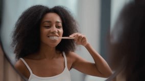 Reflection in mirror African American woman holding toothbrush brushing white teeth biracial girl female cleaning mouth oral hygiene procedure morning dental care routine whitening tooth with brush - Powered by Shutterstock - Get 15% off with code: PIKWIZARD15