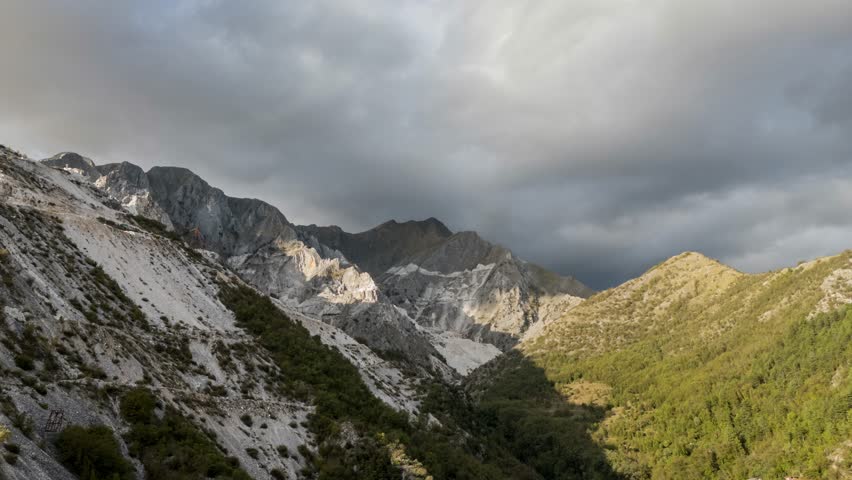 Majestic mountain range in Tuscany with sunlit peaks and looming clouds, aerial hyperlapse